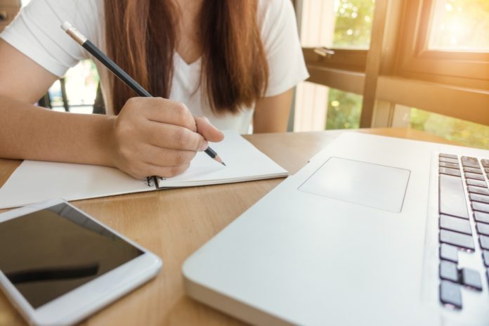 Etudiante travaille à l'écrit devant son ordinateur et son téléphone